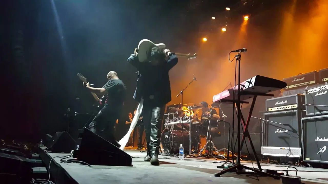 Mateo Acevedo levanta su guitarra sobre la cabeza en un show de rock con amplificadores en la tarima.