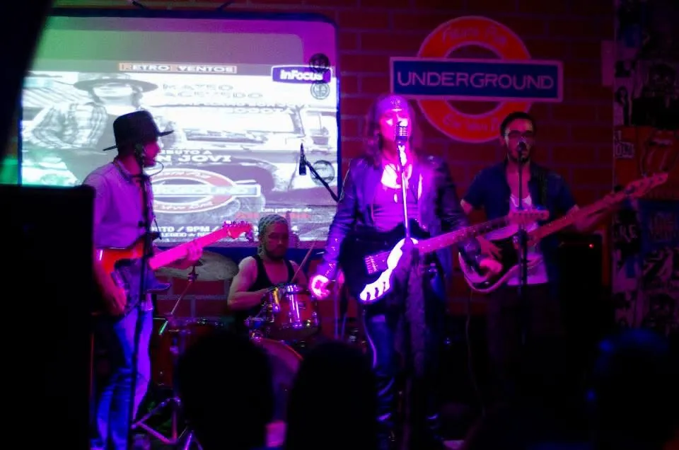 Mateo Acevedo y su banda en un show tributo de rock en vivo, con afiche proyectado en pantalla detrás.