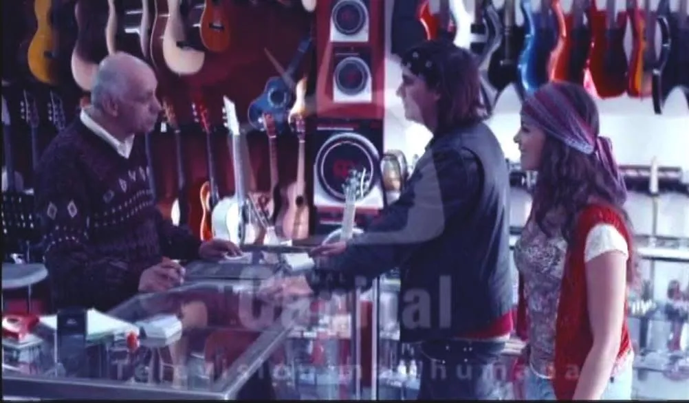 Mateo Acevedo en una tienda de guitarras atendido por el vendedor, rodeado de instrumentos colgados.